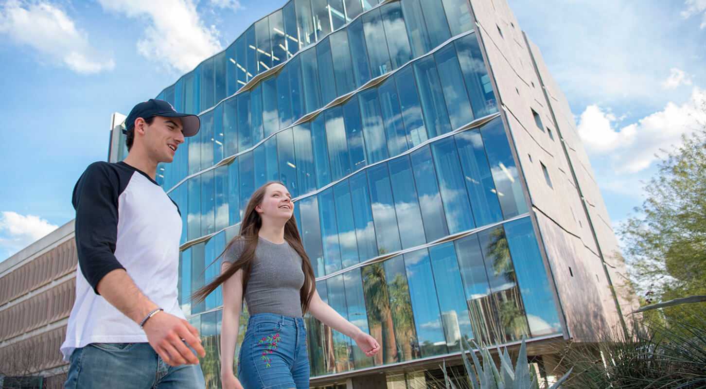 Two students walking in front of a building with reflective glass
